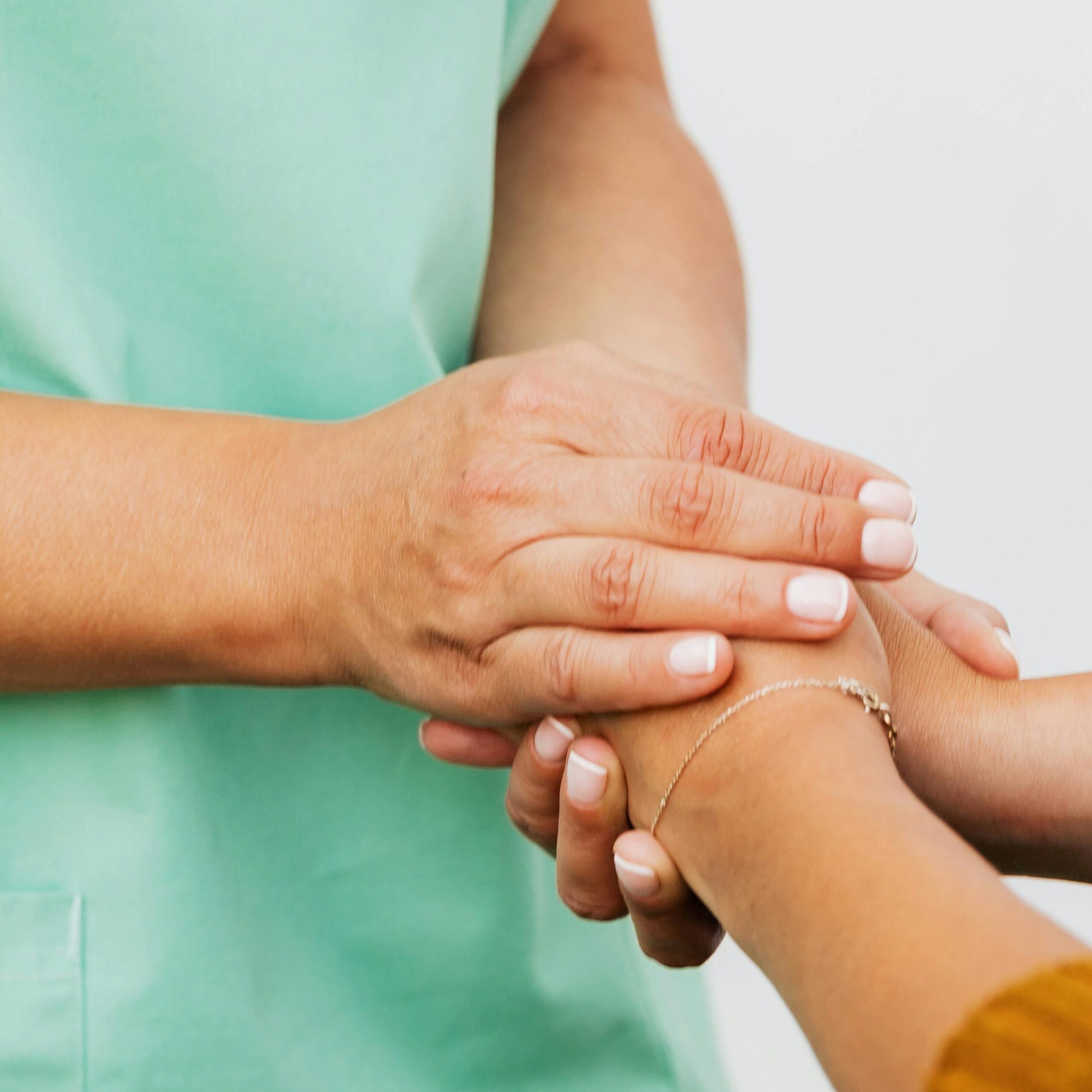 A nurse in green scrubs gently clasps a patient's hand, offering support.